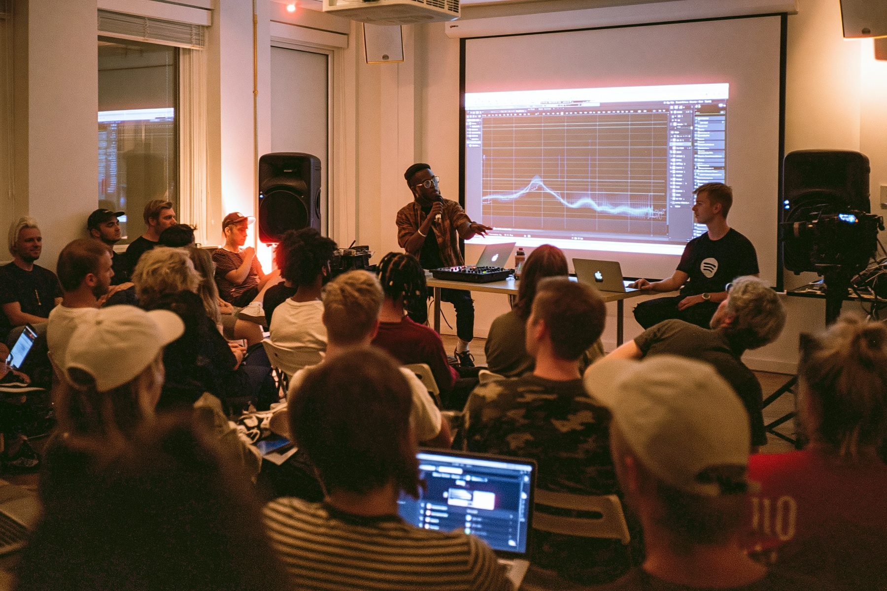 A presenter speaking in front of a projected waveform at the MPC's Spotify masterclass
